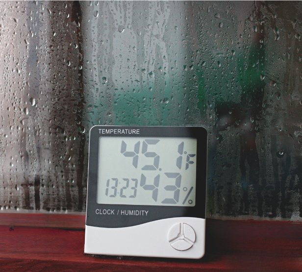 Digital hygrometer showing indoor humidity levels beside a window with condensation